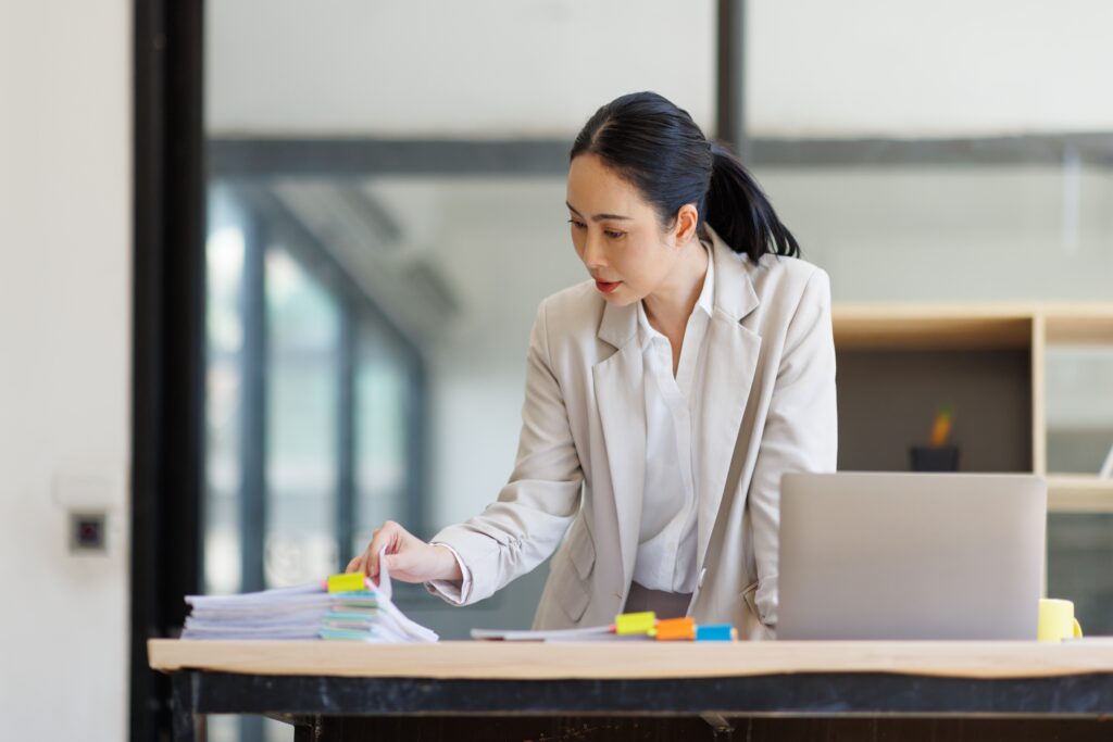 Woman reviewing documents beside a laptop in a modern office.